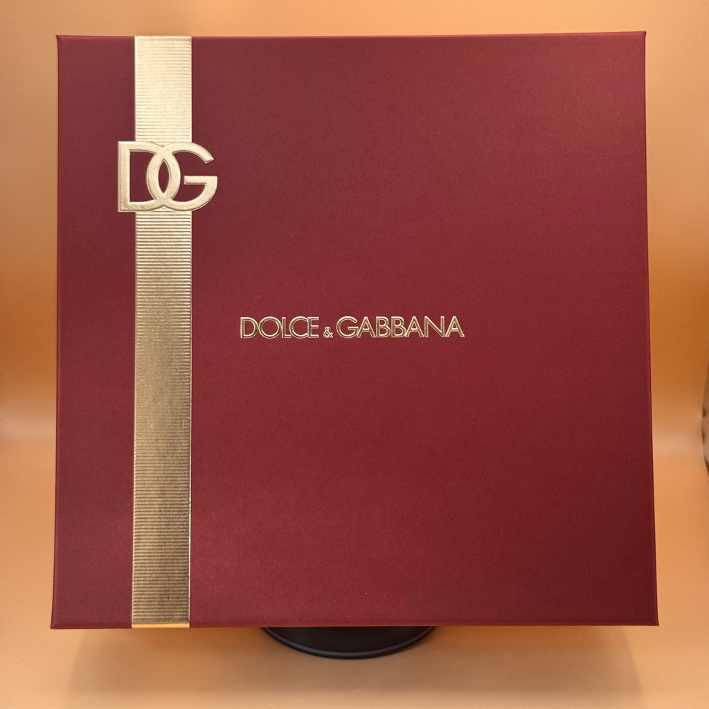 Dolce & Gabbana box with gold ribbon and logo on a beige background