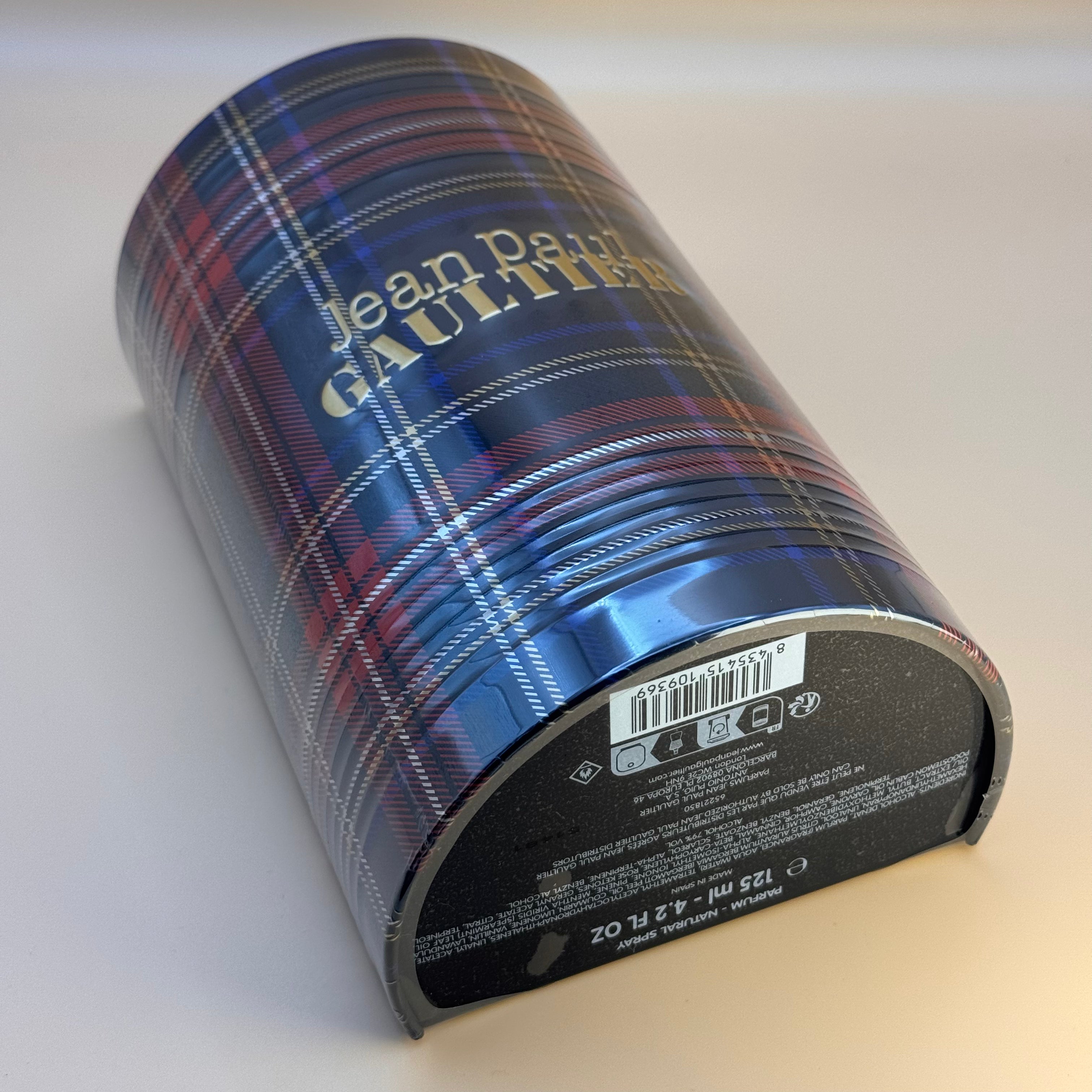 Cylindrical packaging with plaid design and 'Jean Paul Gaultier' branding on a white background
